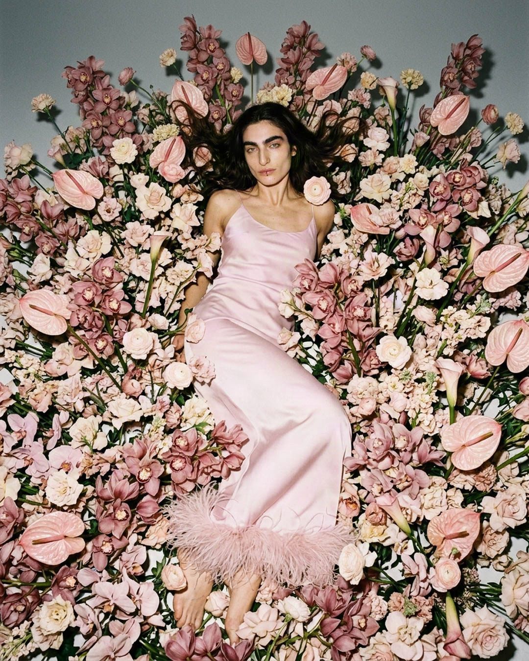 MISHIMONO spec editorial model in a pale pink slip dress reclining within a wall of blush flowers
