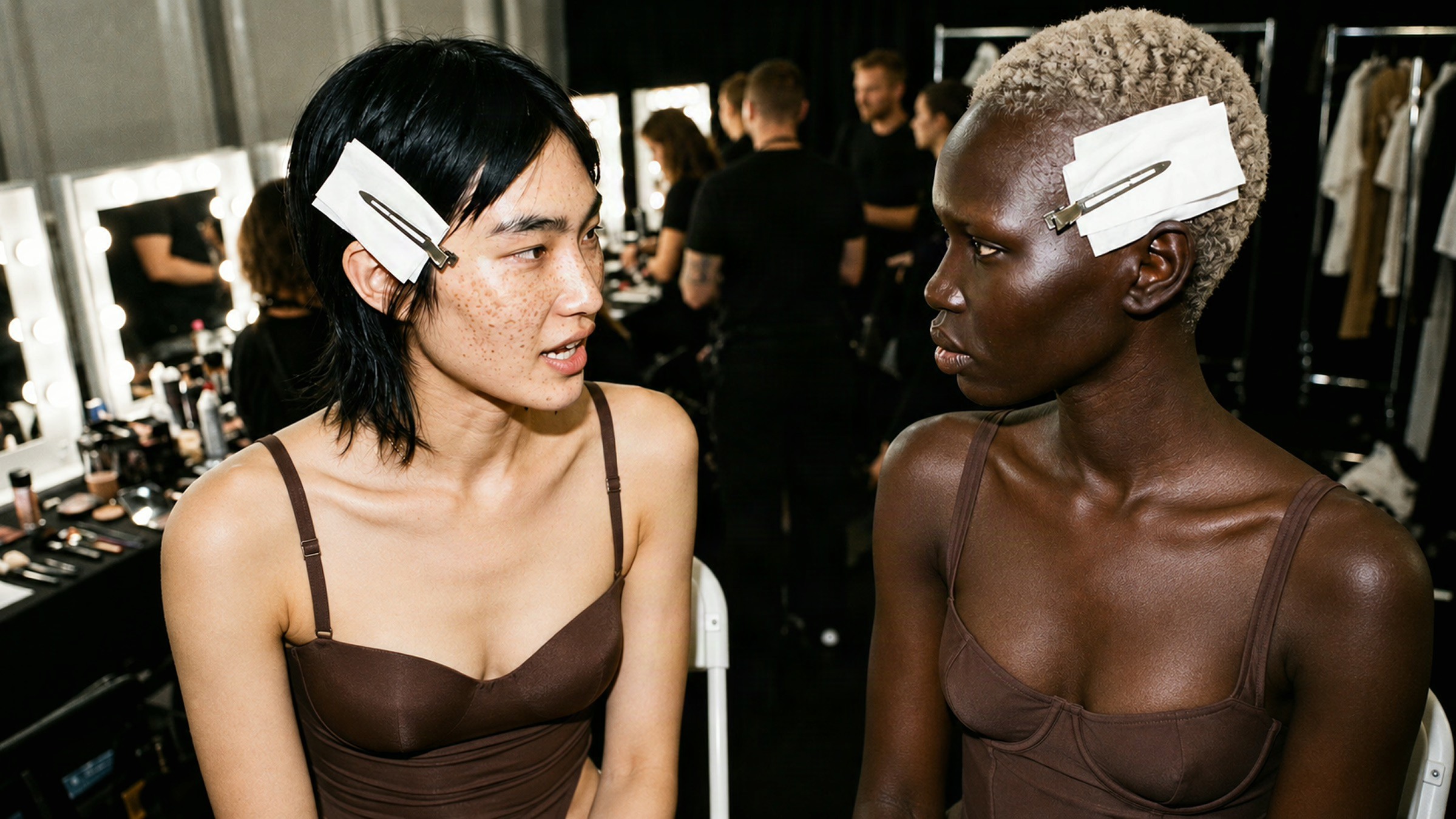 SKIMS spec editorial backstage close-up of two models in brown lingerie-inspired looks and pinned hair