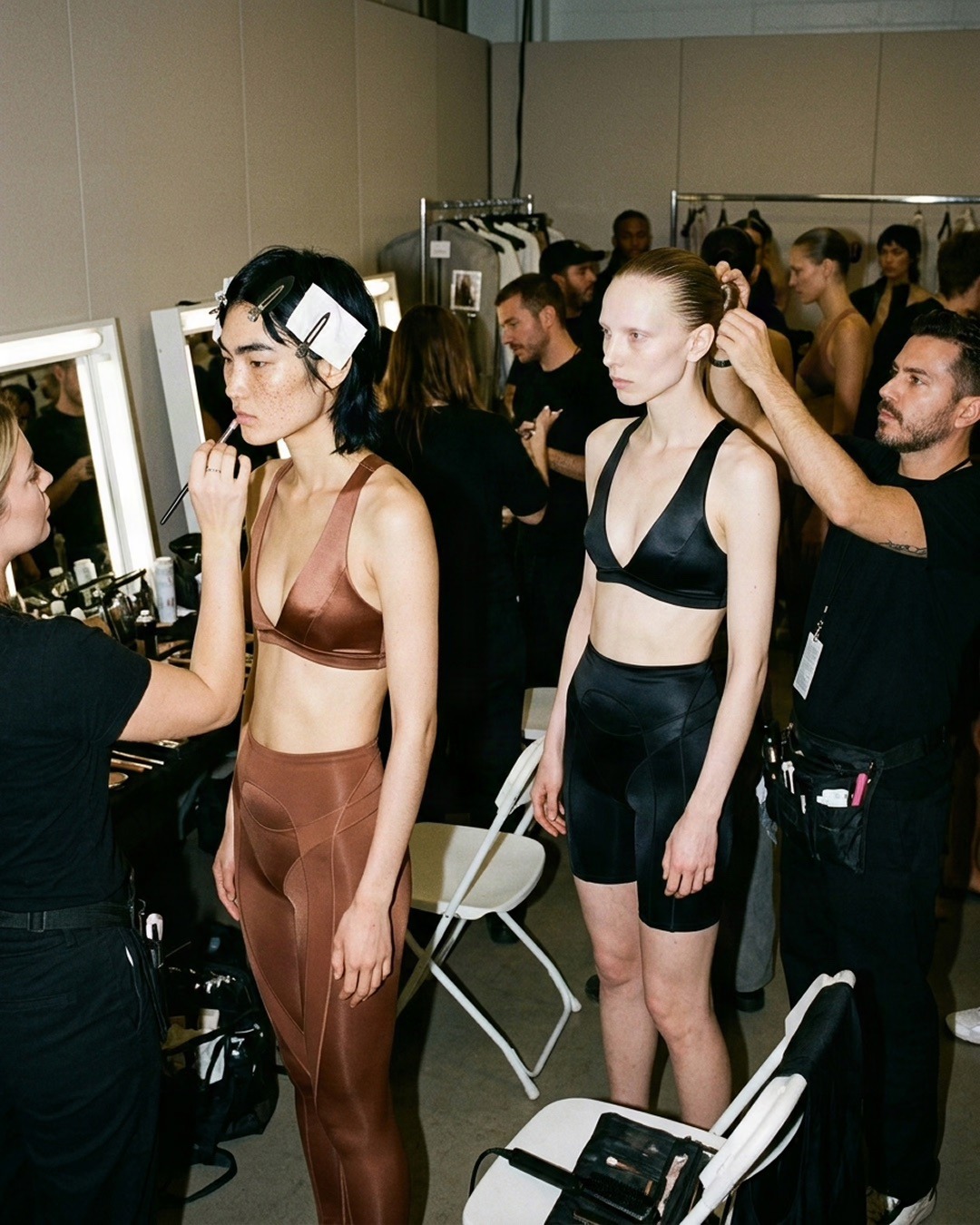 SKIMS spec editorial backstage scene with two models in sculpted brown and black bodywear before makeup
